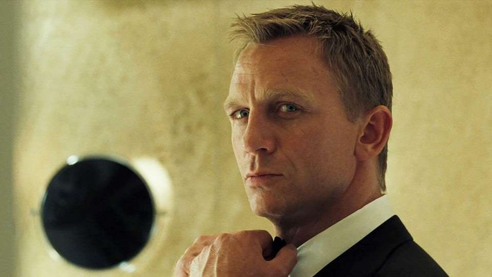 Portrait rapproché de Daniel Craig dans le rôle de James Bond. Il regarde à l'oblique, et replace son nœud papillon avec ses mains.