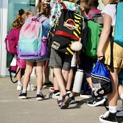 Des élèves du primaire entrant en classe avec un sac à dos.