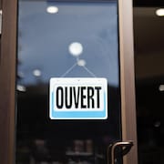 Un panneau « Ouvert » accroché sur une porte vitrée.