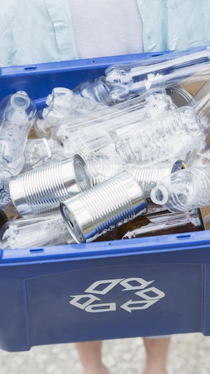 Quelqu'un tient un bac de recyclage bleu rempli de bouteilles de plastique vides.