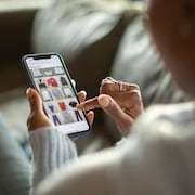 Une femme en train de magasiner en ligne sur son téléphone intelligent dans son salon.