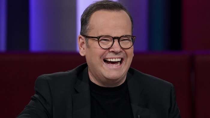 Assis dans le studio, l'homme éclate de rire.