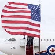 Mark Carney descend les marches d'un avion caché par un drapeau américain.