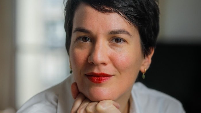 Portrait de Marie-Eve Lacasse qui fixe la caméra, la tête appuyée sur les jointures de sa main droite.