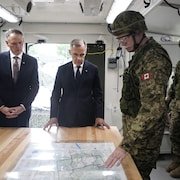 Trois hommes, dont un portant un uniforme militaire, debout autour d'une carte.