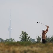 Un golfeur devant la Tour du CN floue en raison de la fumée des incendies de forêt, le 14 juillet 2025.