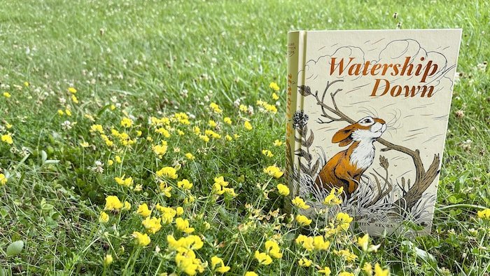 La bande dessinée «Watership Down» de James Sturm et Joe Sutphin, déposée sur du gazon et des fleurs.