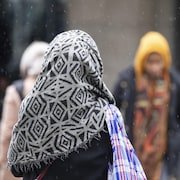 Une femme portant un voile marche sous une fine neige, à Montréal.