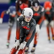 Une patineuse de vitesse, les mains sur les genoux, sourie après une course.