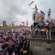 Des manifestants brandissent des drapeaux et grimpent sur une statue près de la Tamise, à Londres.